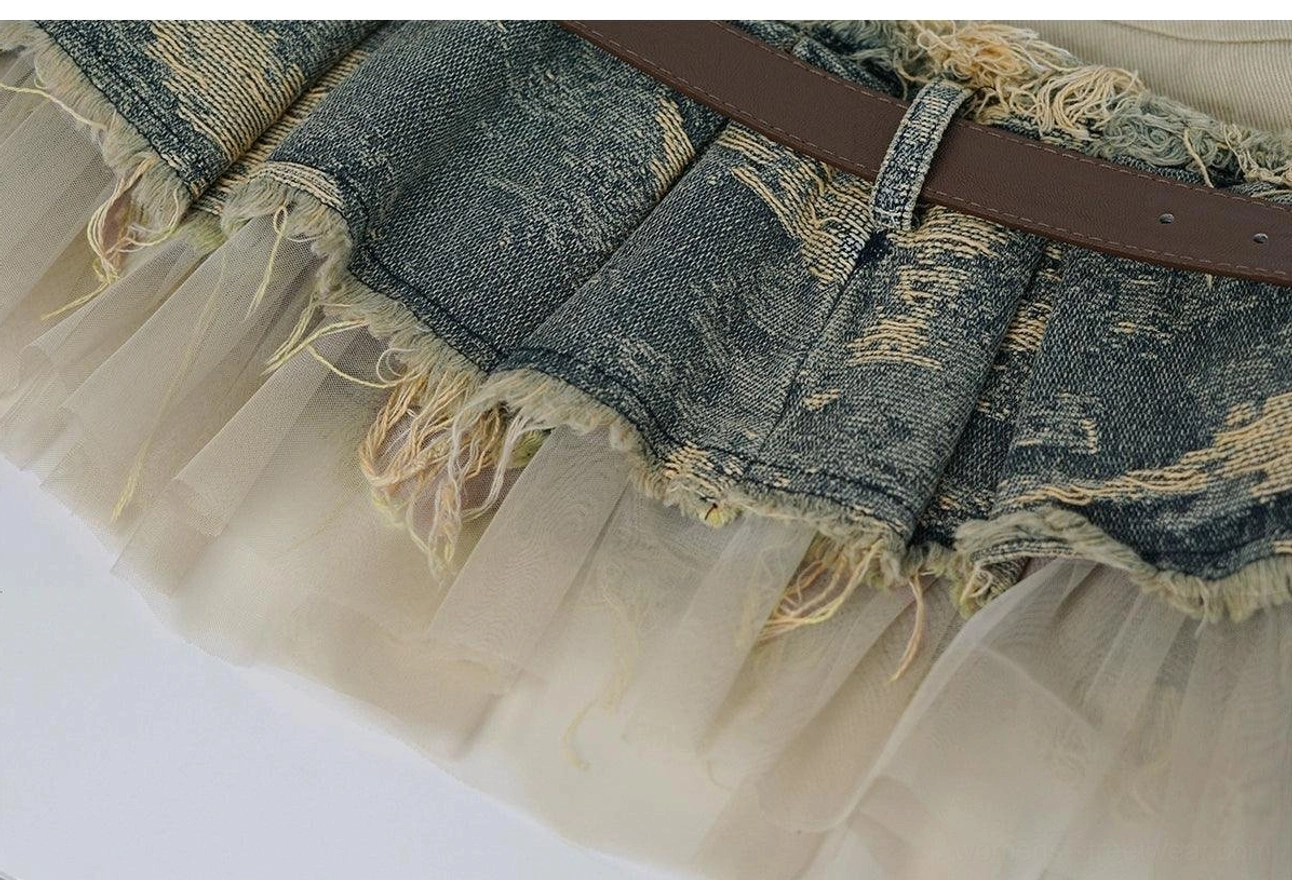 Close-up of a layered distressed denim mini skirt hem with pleated fabric, sheer tulle underlayer, raw edges, and brown leather belt