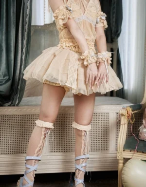 Layered lace tulle mini skirt styled in a vintage lolita bedroom with beige ruffled mesh layers, lace leg wraps, and matching lace wrist cuffs