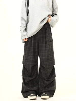 Front view of charcoal gray plaid wide-leg streetwear pants styled with an oversized gray sweatshirt canvas sneakers and crossbody bag