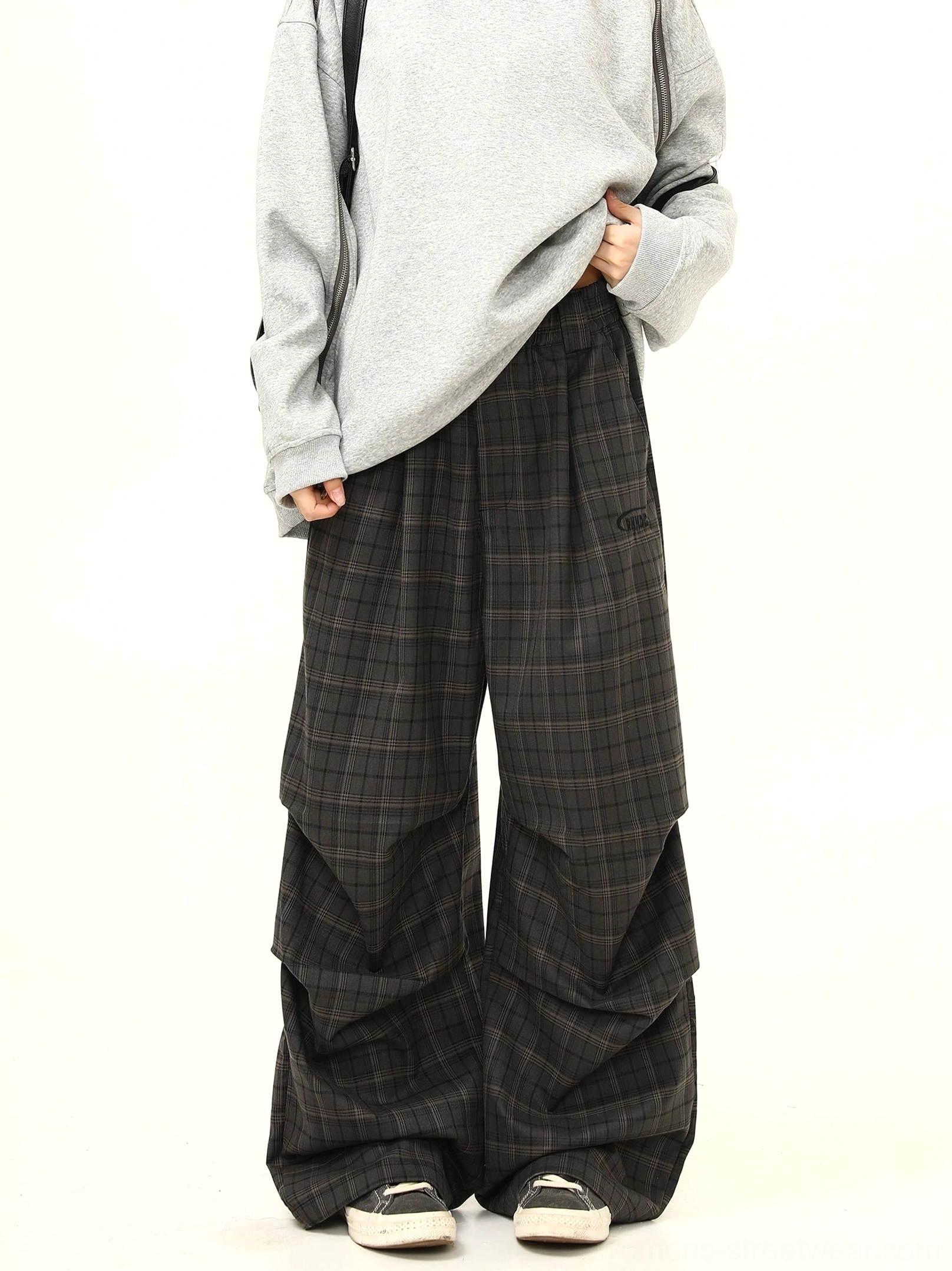 Front view of charcoal gray plaid wide-leg streetwear pants styled with an oversized gray sweatshirt canvas sneakers and crossbody bag