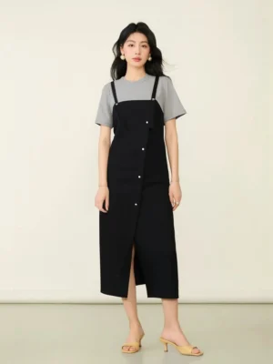 Front full-body view of a layered tee pinafore midi dress with grey short-sleeve T-shirt, black overall skirt, diagonal metal buttons, and side split hem