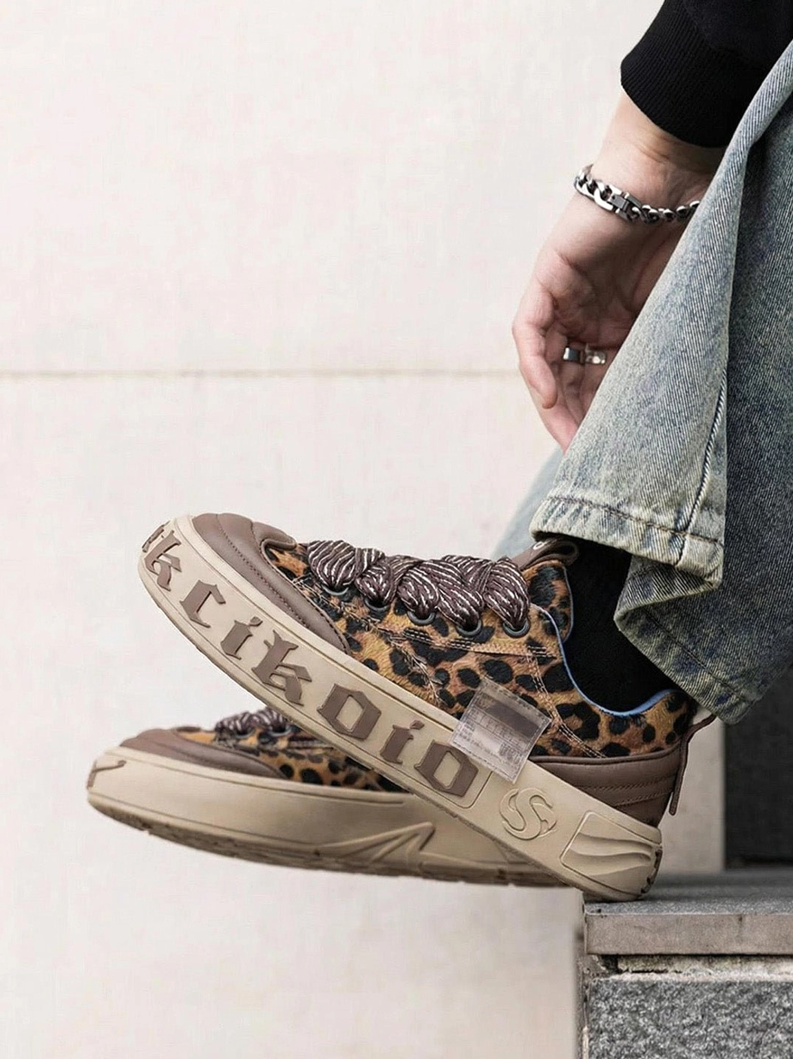 Leopard print chunky skate sneakers worn with jeans in a casual streetwear outfit on stone steps