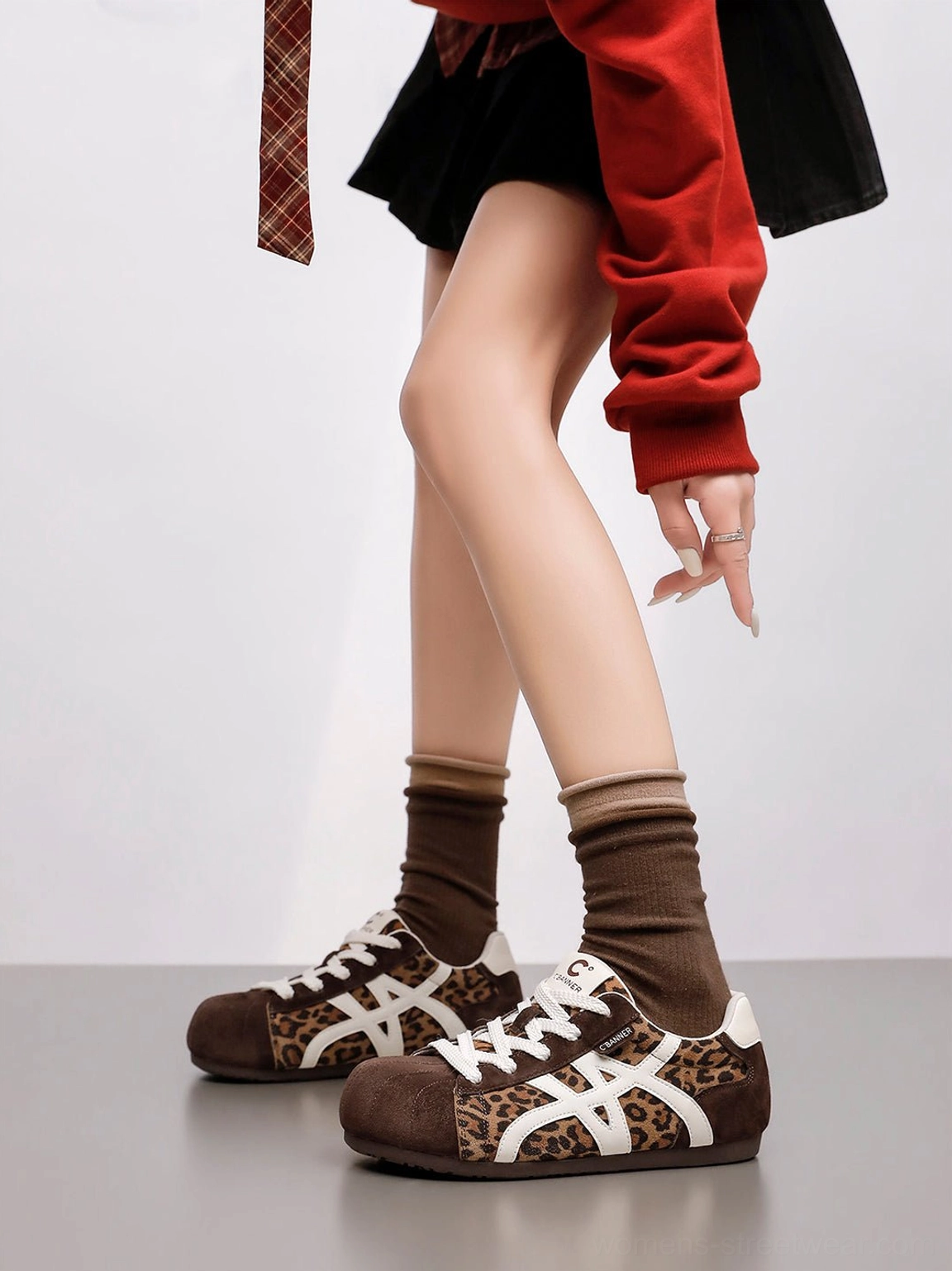 Side on-foot view of leopard panel gum sole retro trainers for women with brown crew socks and mini skirt