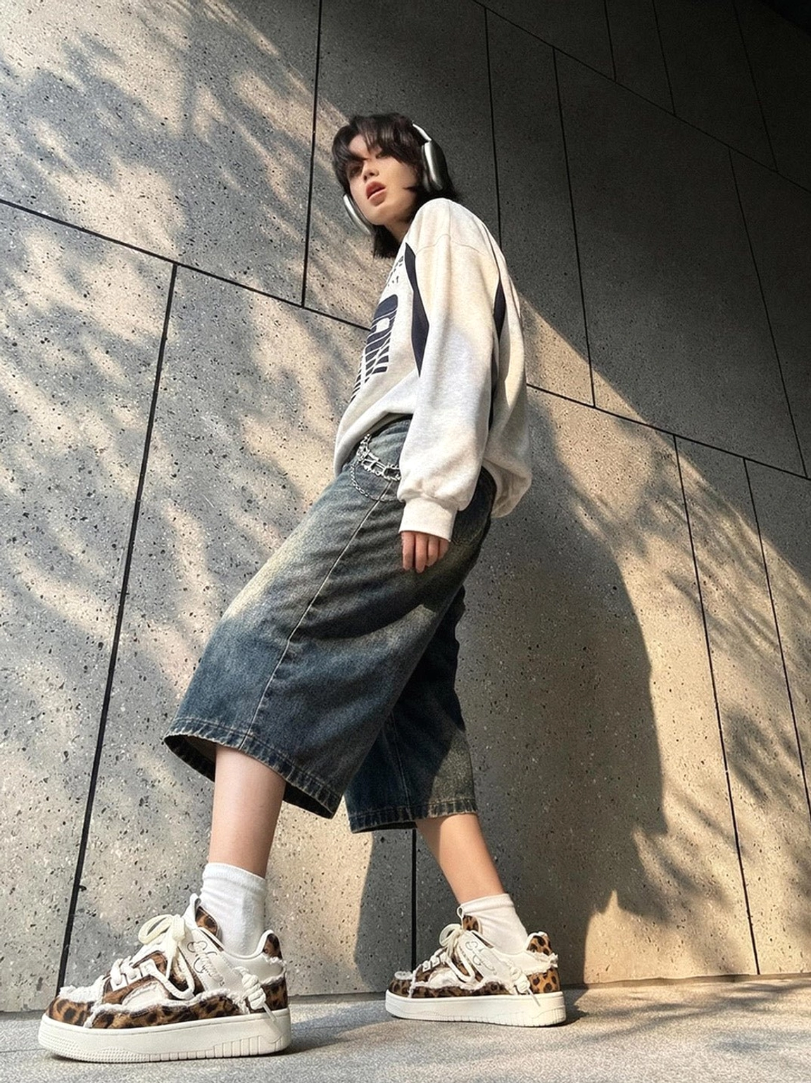 Model wearing leopard print deconstructed platform canvas sneakers with an oversized graphic sweatshirt, cropped wide-leg denim, white socks, and headphones in a Seoul-inspired streetwear outfit
