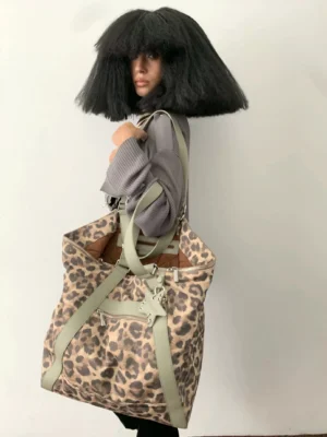 Leopard print commuter tote bag with sage green leather straps carried by model in indoor studio