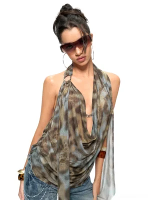 Front view of a leopard print cowl halter top with deep plunge neckline, metal neck ring, flowing draped fabric, and long side sashes styled with denim jeans