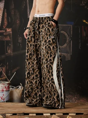 Three quarter side view of leopard print streetwear track pants showing wide legs white double side stripes and pocket