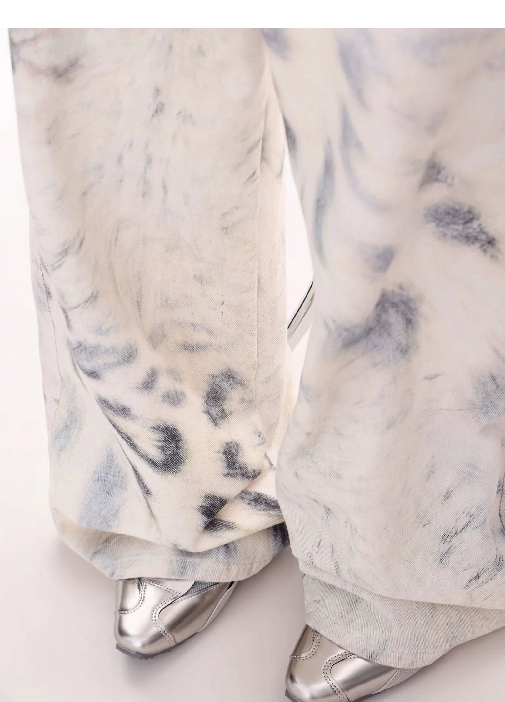 Close-up of the stacked wide-leg hem on leopard tie-dye jeans styled with silver pointed-toe shoes