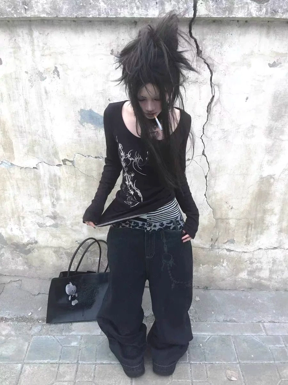 Front low angle view of black leopard waistband chain baggy jeans styled on a punk streetwear model against a weathered concrete wall