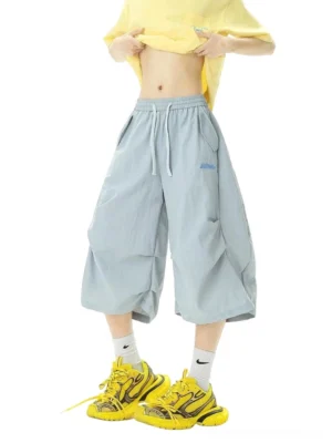 Light ash blue wide-leg balloon jogger shorts in crinkled nylon with elastic drawstring waist and embroidered side detail styled with a cropped top and sporty sneakers