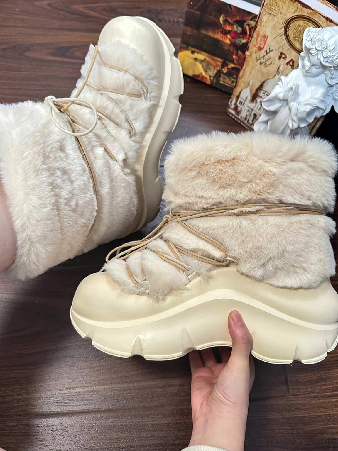 Light beige faux fur platform snow boot held by hand to show the chunky sole height and decorative beaded drawstring details