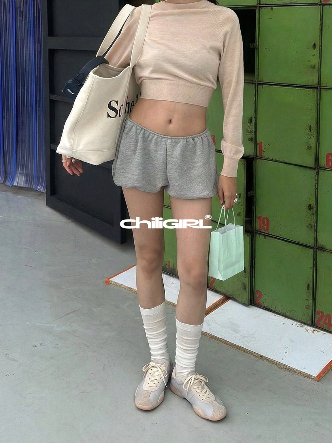 Light beige retro streetwear lace-up trainers styled with grey shorts, a cropped knit top, and sheer white socks in an industrial setting