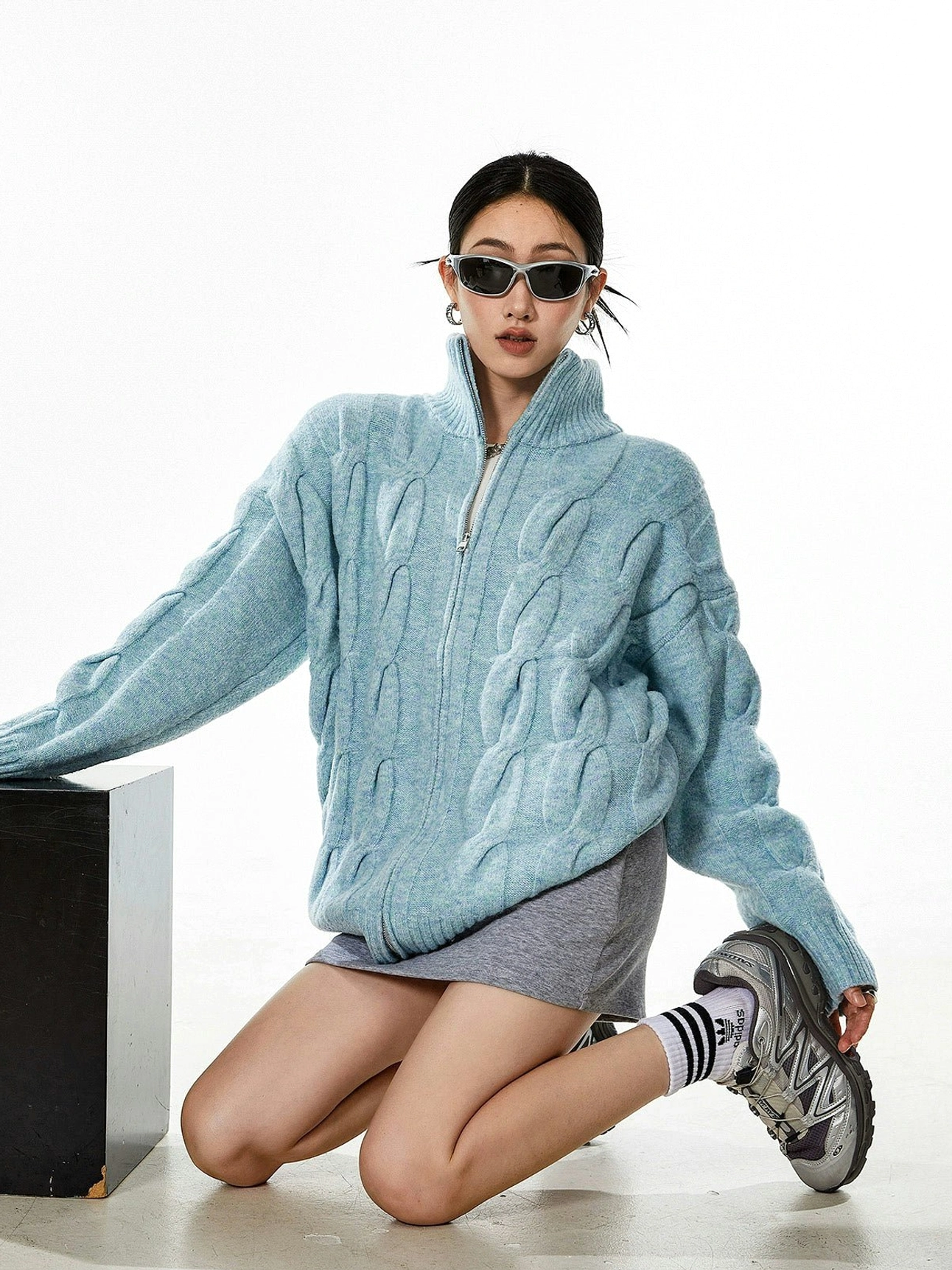 Light blue oversized cable knit cardigan layering with mini skirt athletic sneakers street style