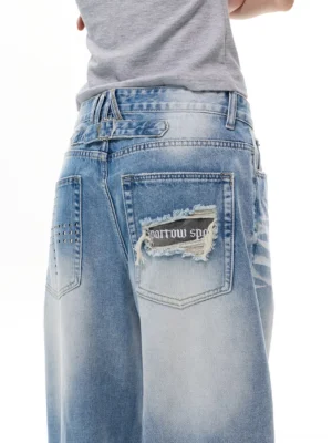 Close-up of the distressed frayed back pocket and metal stud details on light blue wide-leg denim jeans
