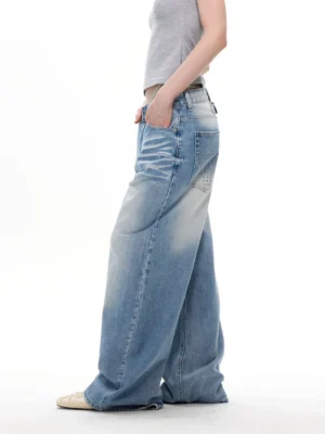 Light blue distressed studded wide-leg denim jeans shown in a side rear three-quarter view with a relaxed baggy fit