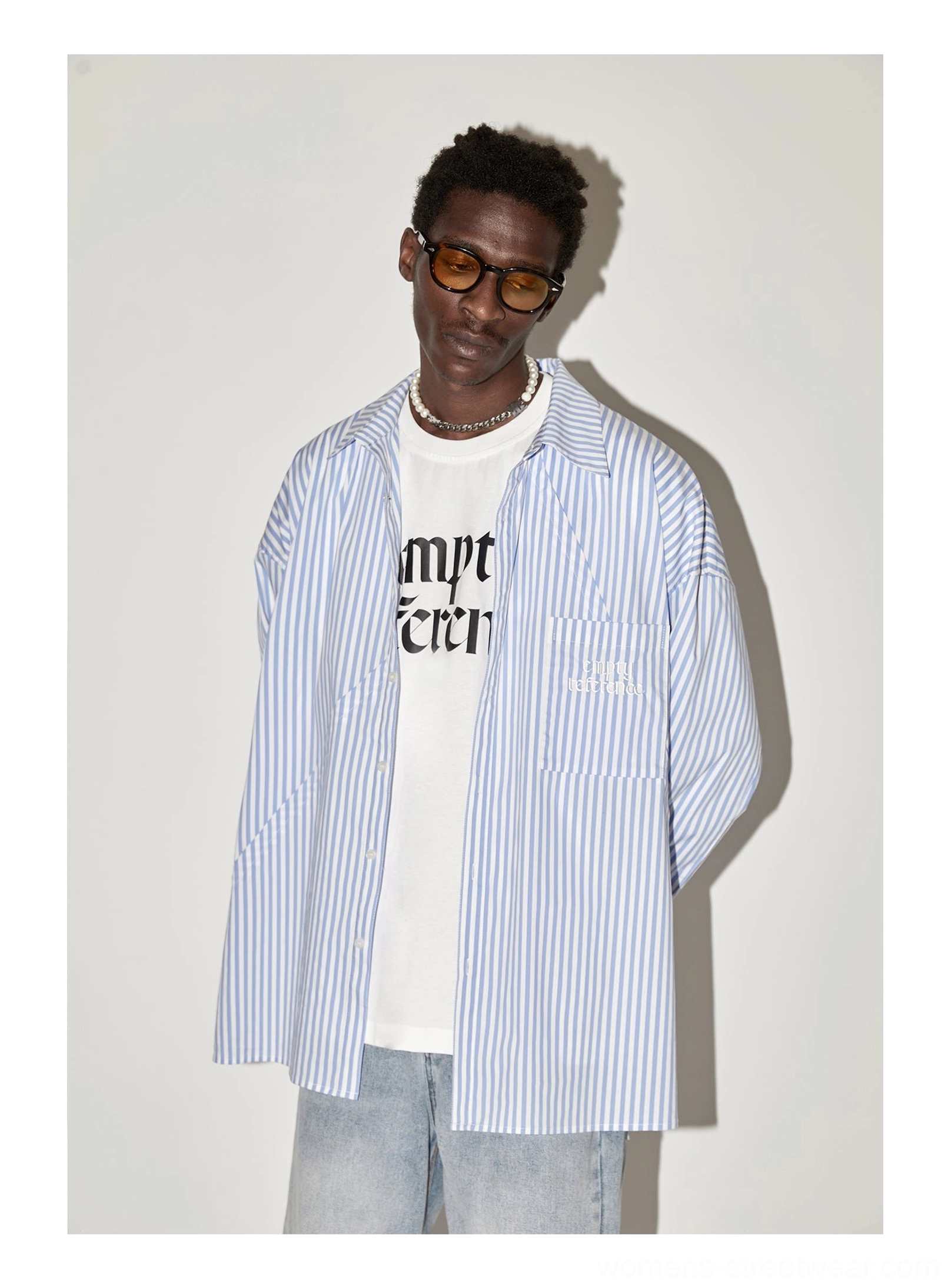 Male model wearing light blue geometric panel striped oversized streetwear shirt layered over graphic tee and light wash jeans