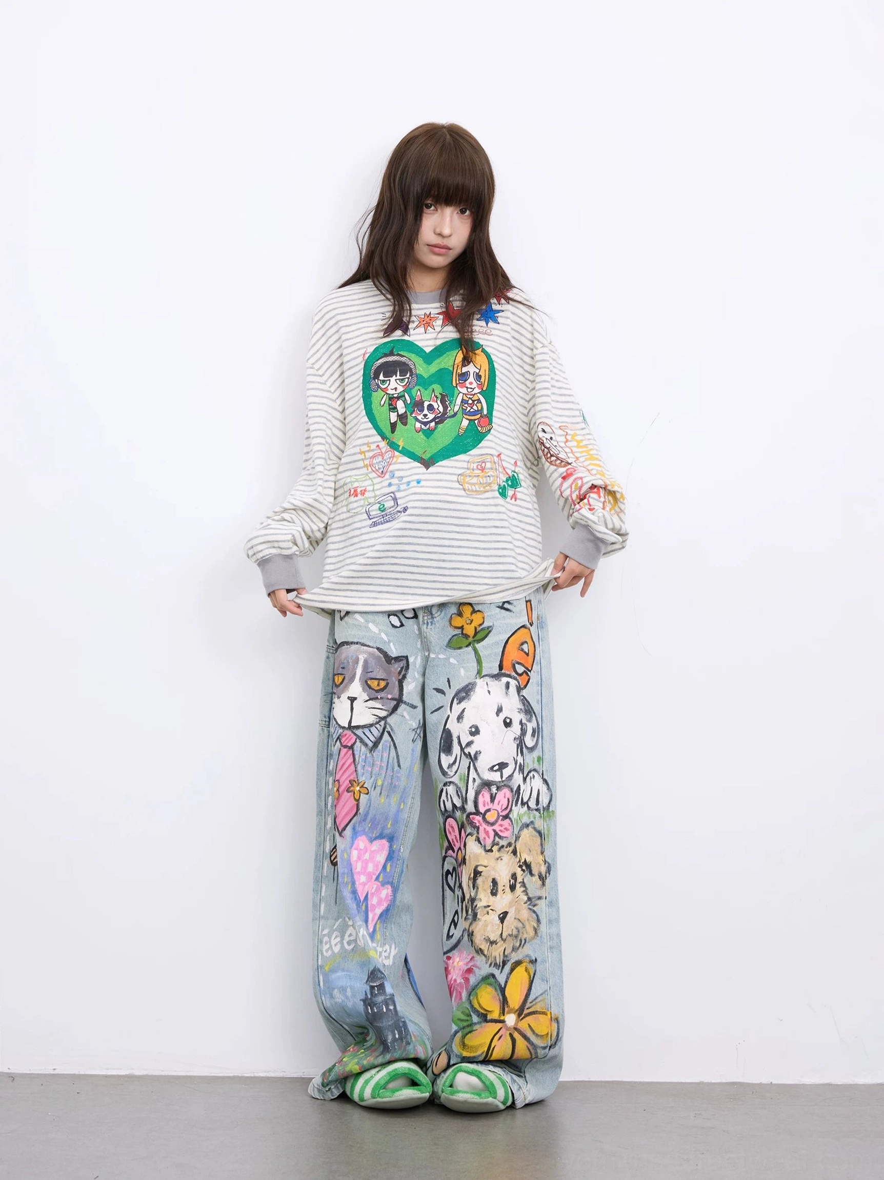 Front view of relaxed light blue streetwear jeans with playful hand-drawn graffiti artwork styled with a striped top and casual flats