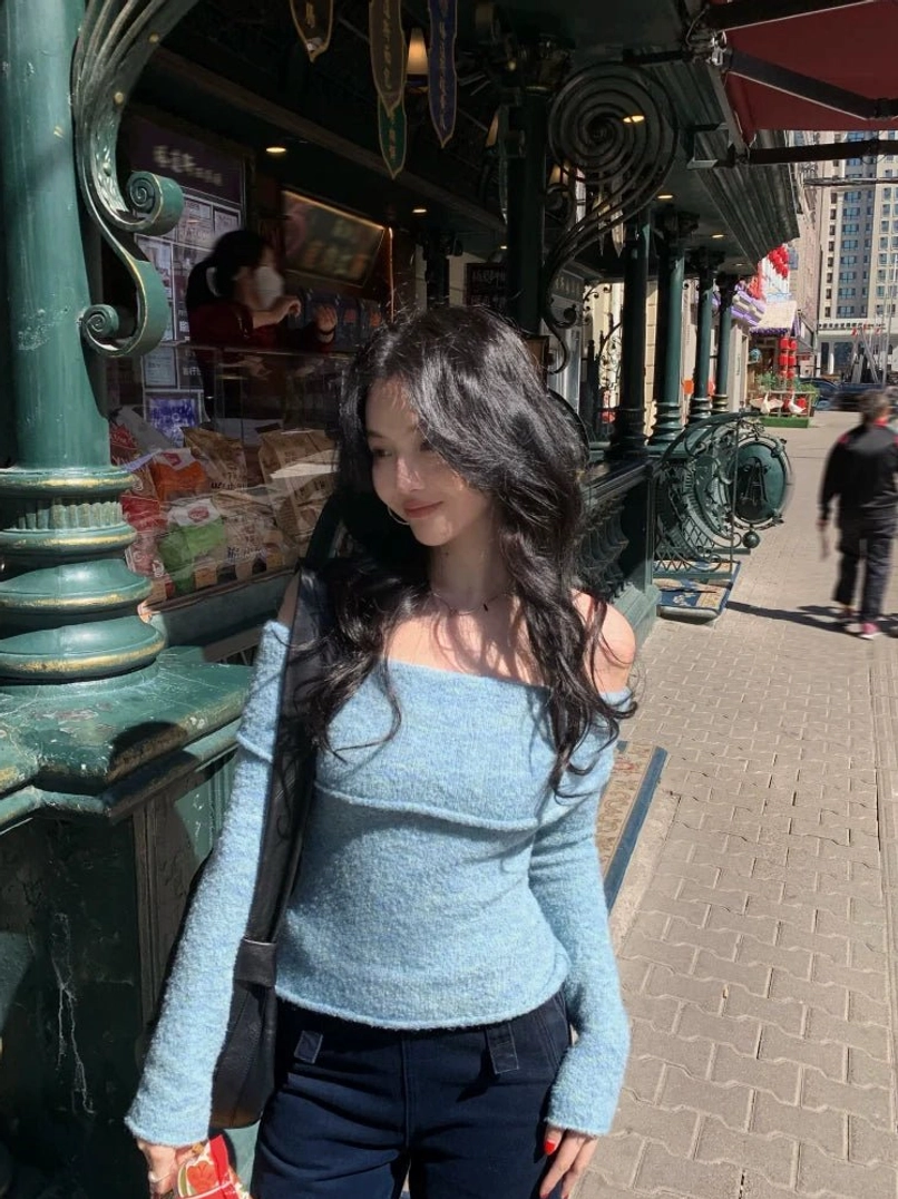 Light blue heathered off-shoulder knit sweater top shown in a three-quarter street style view with fitted long sleeves