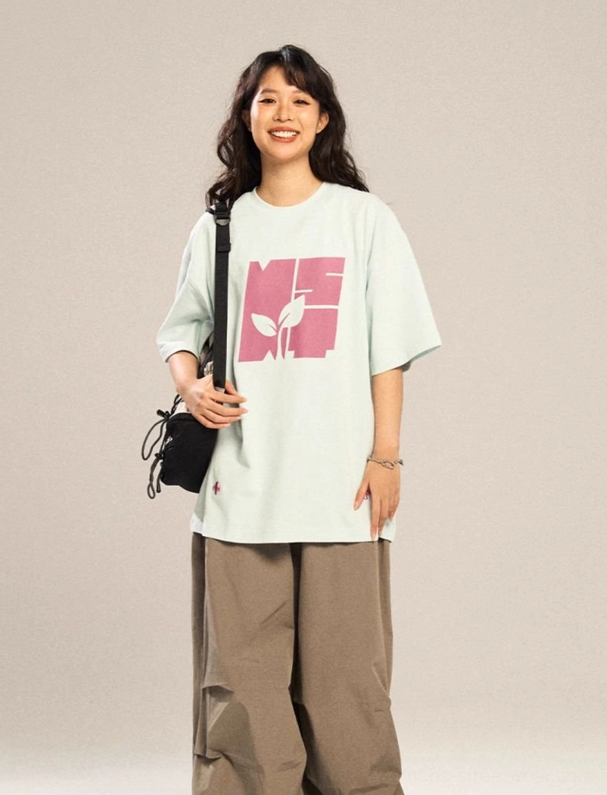 Light blue oversized graphic T-shirt with pink contrast botanical logo, subtle cross embroidery, and relaxed Seoul streetwear silhouette