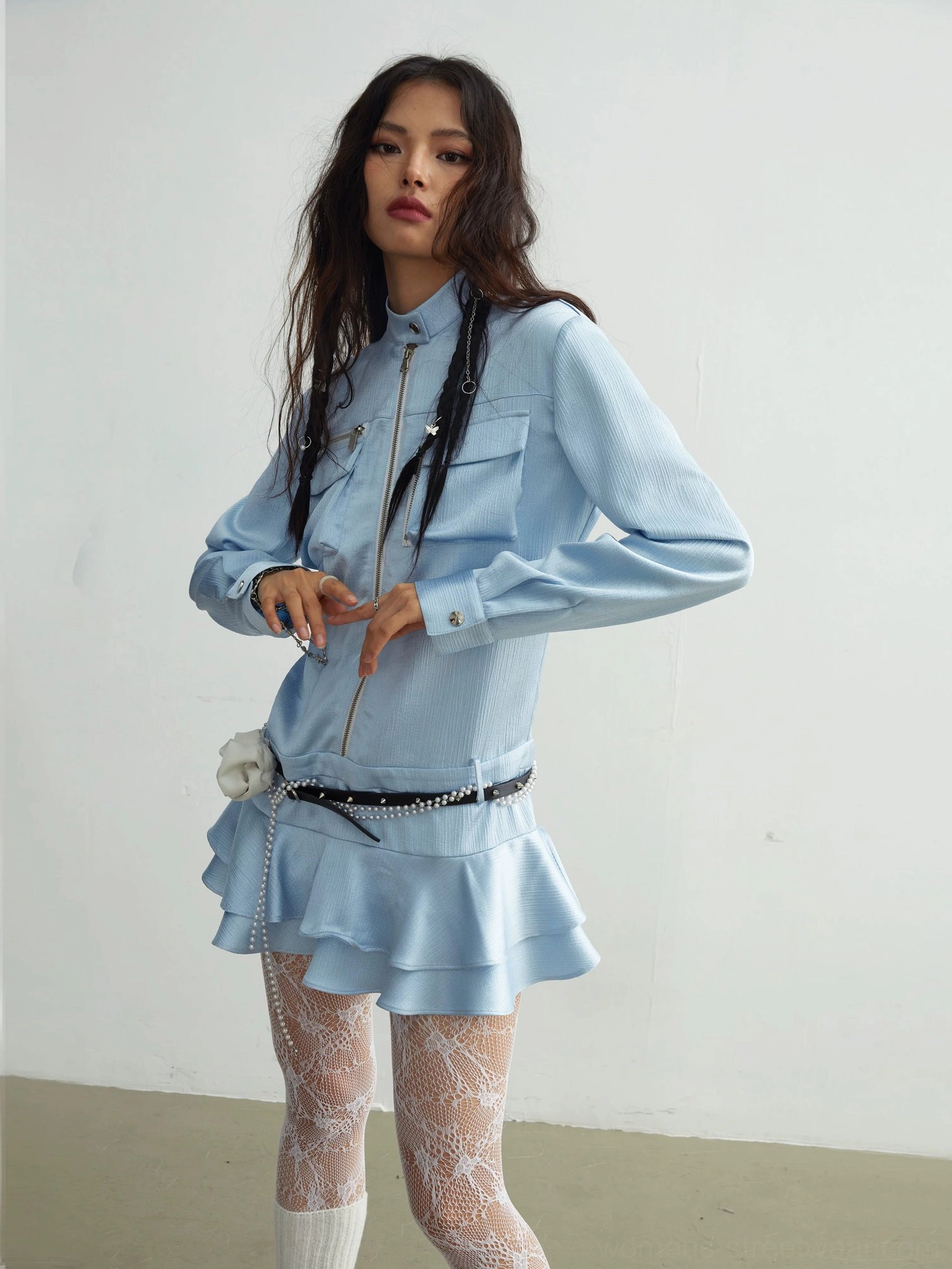Three-quarter front view of a light blue ruffle mini dress with satin-look fabric, tiered skirt, lace tights, pearl belt, and flower accent