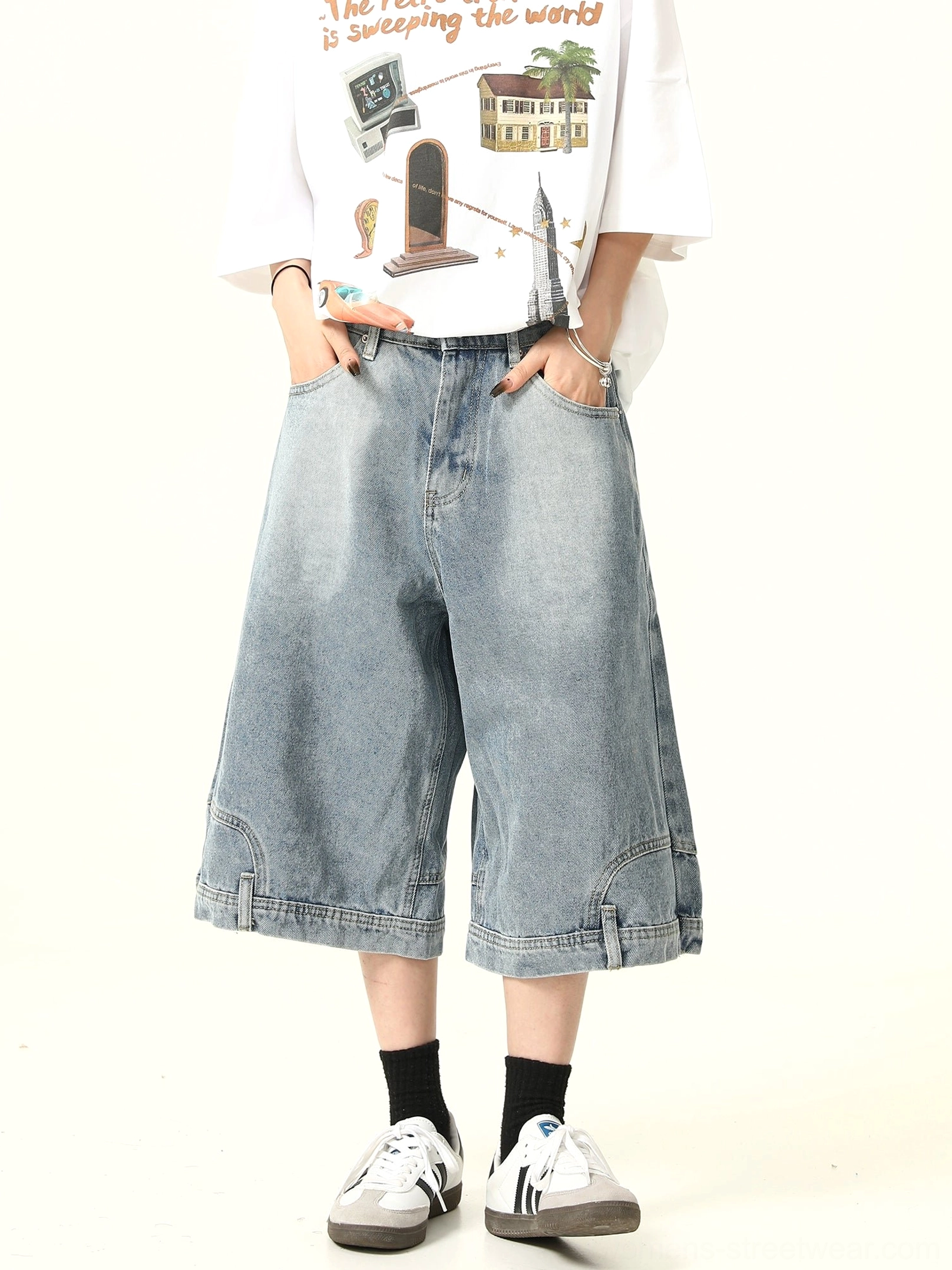 Full front view of relaxed light blue washed denim culotte shorts with loose straight wide legs, belt loops, graphic T-shirt, black socks, and casual sneakers