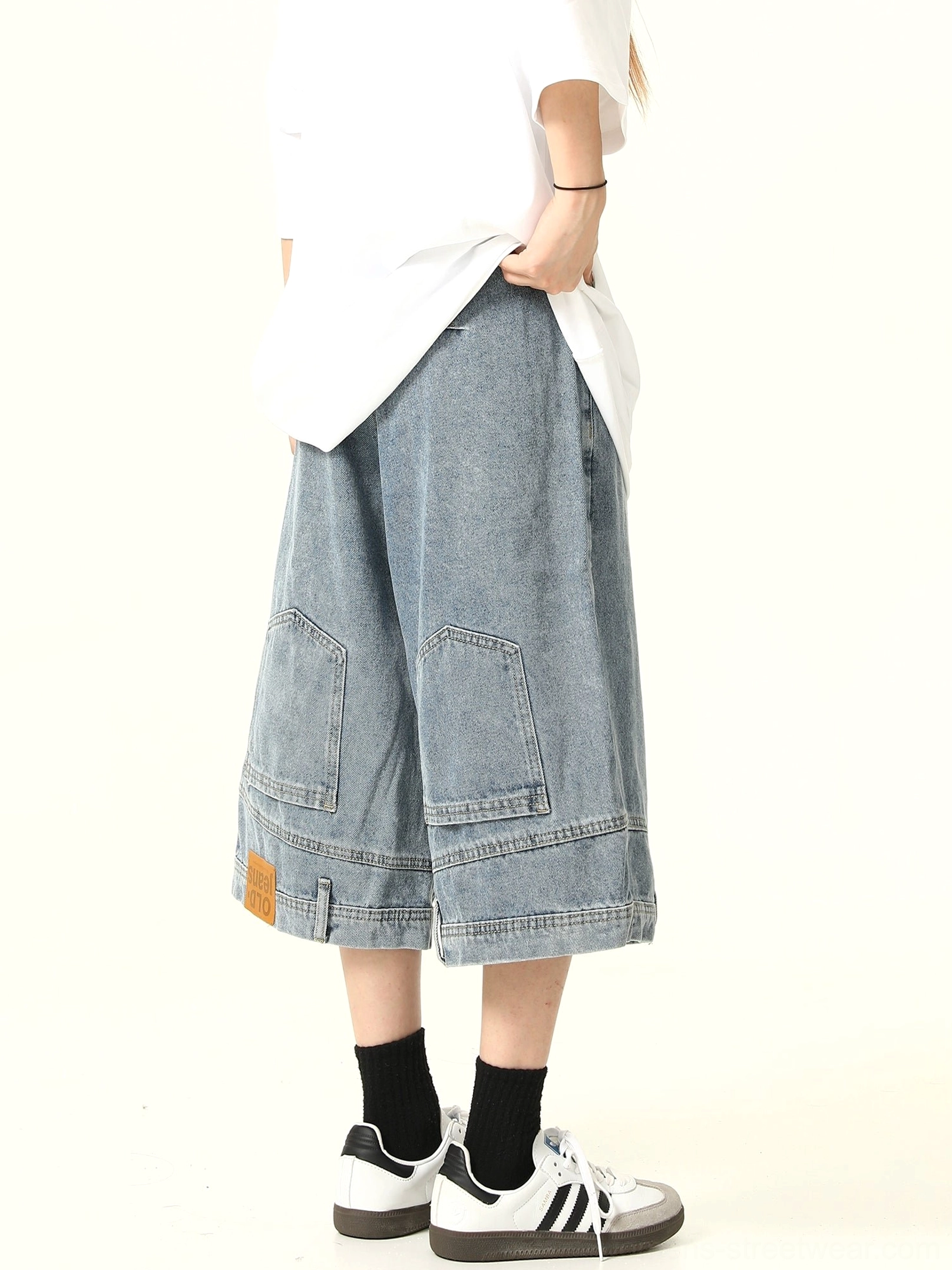 Rear full view of light blue wide-leg denim culotte shorts with dual cargo-style back pockets, hem patch, oversized white T-shirt, and two-tone sneakers