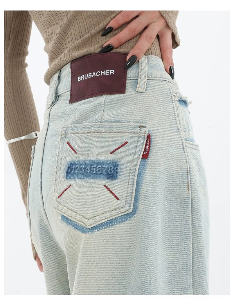 Close-up of the back waist and pocket on light blue wide-leg jeans featuring embroidered number-style artwork and contrast stitching