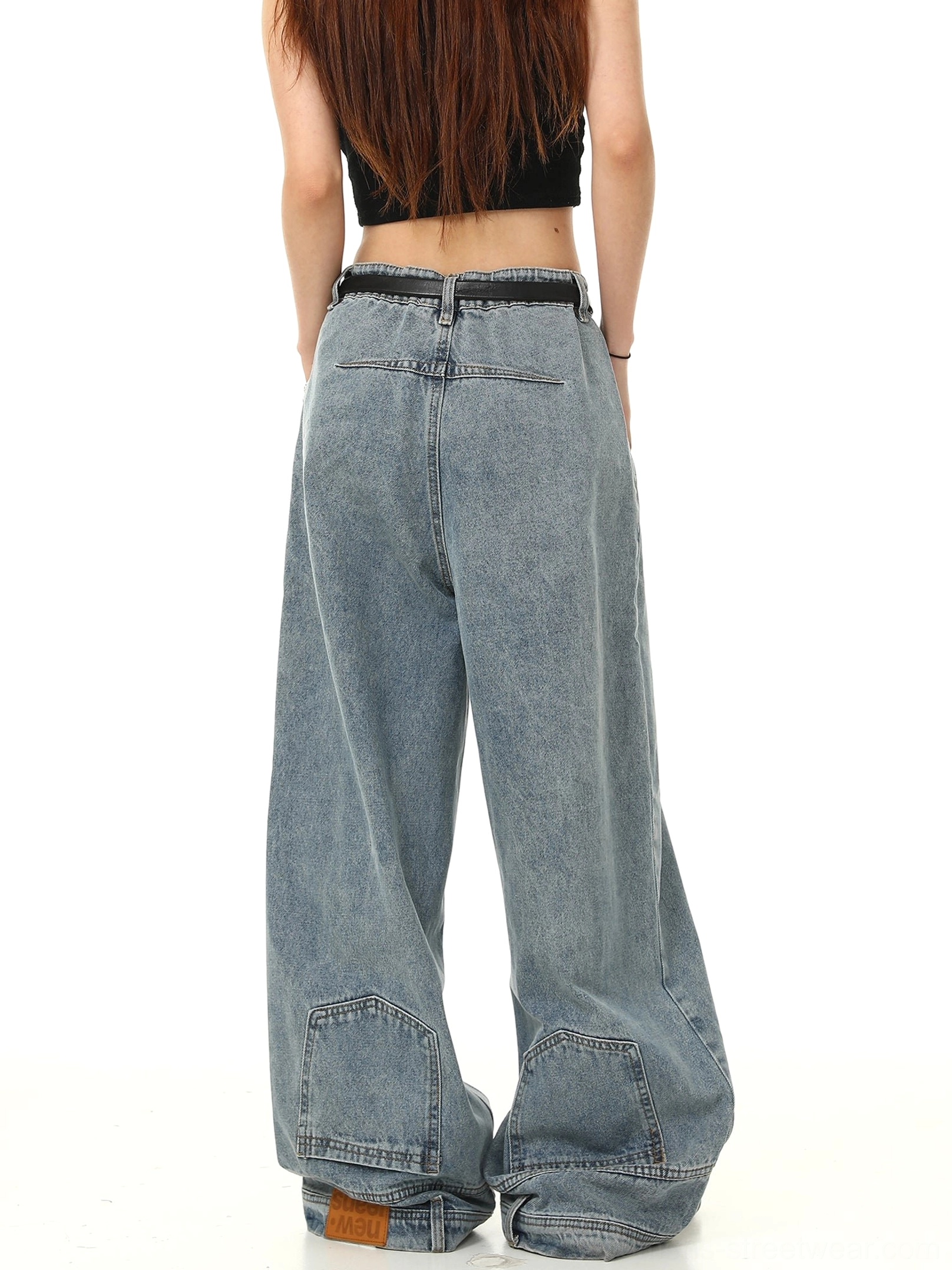 Rear side view of loose light blue Y2K wide-leg jeans with rear pocket detail, long stacked hem, brown hem tag, and black belt