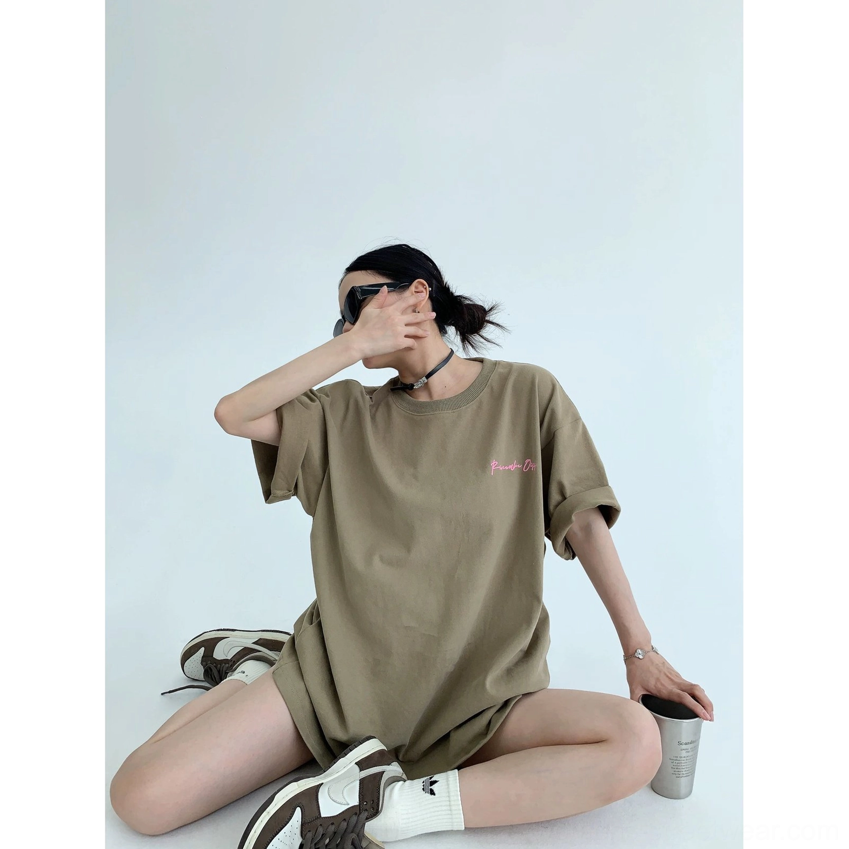 Light brown oversized neon script streetwear T-shirt shown in a seated casual outfit with rolled cuffs, socks, and sneakers