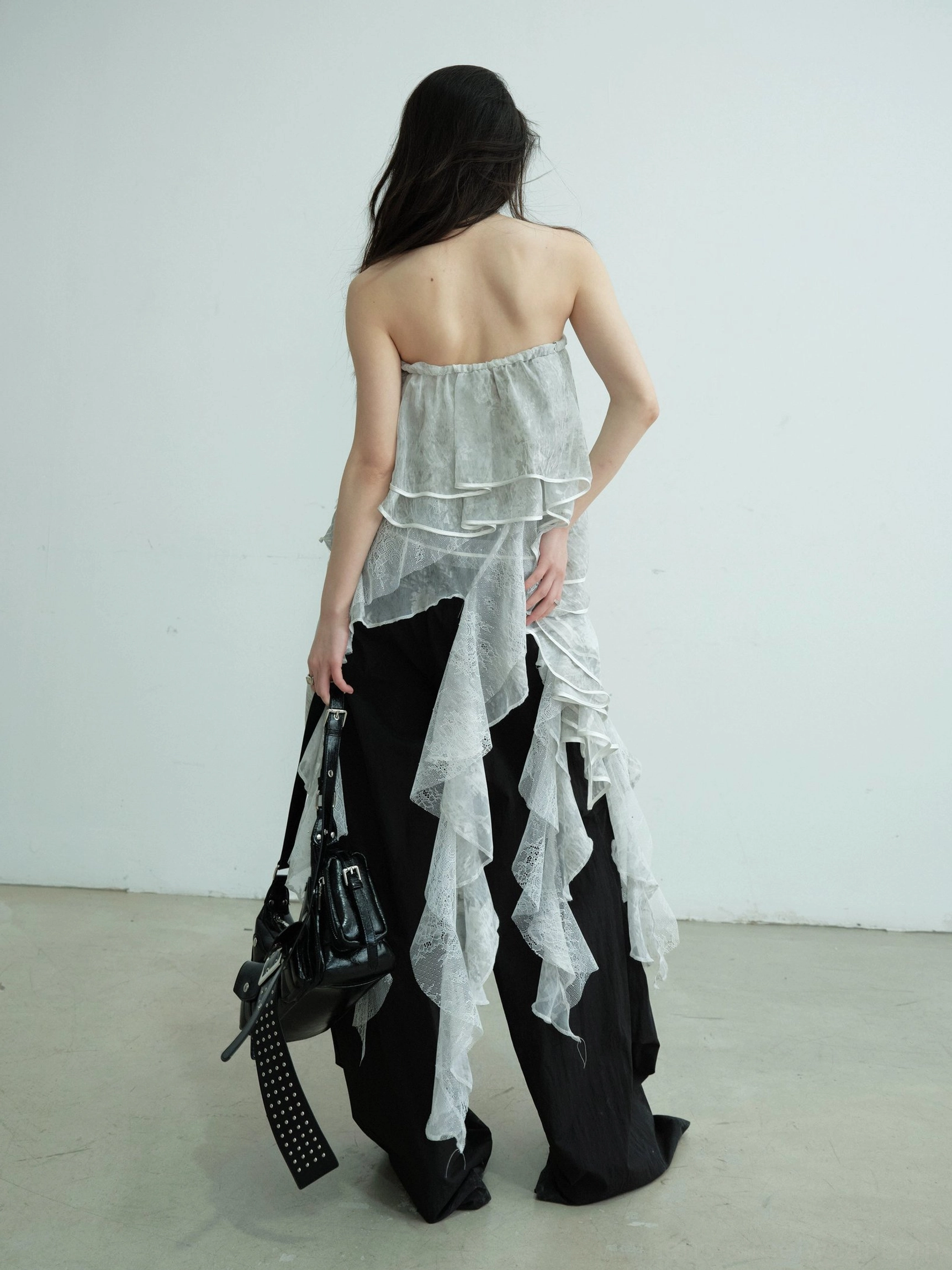 Back view of light gray asymmetric lace ruffle tube top maxi skirt styled as a strapless streetwear layer with long trailing ruffles