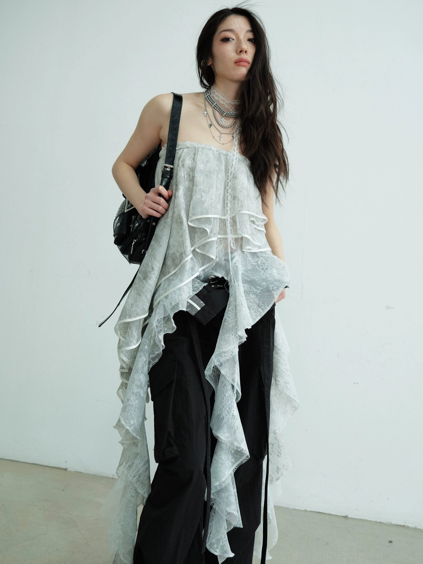 Front full body view of light gray asymmetric lace ruffle tube top maxi skirt styled with black wide leg cargo pants and layered necklaces