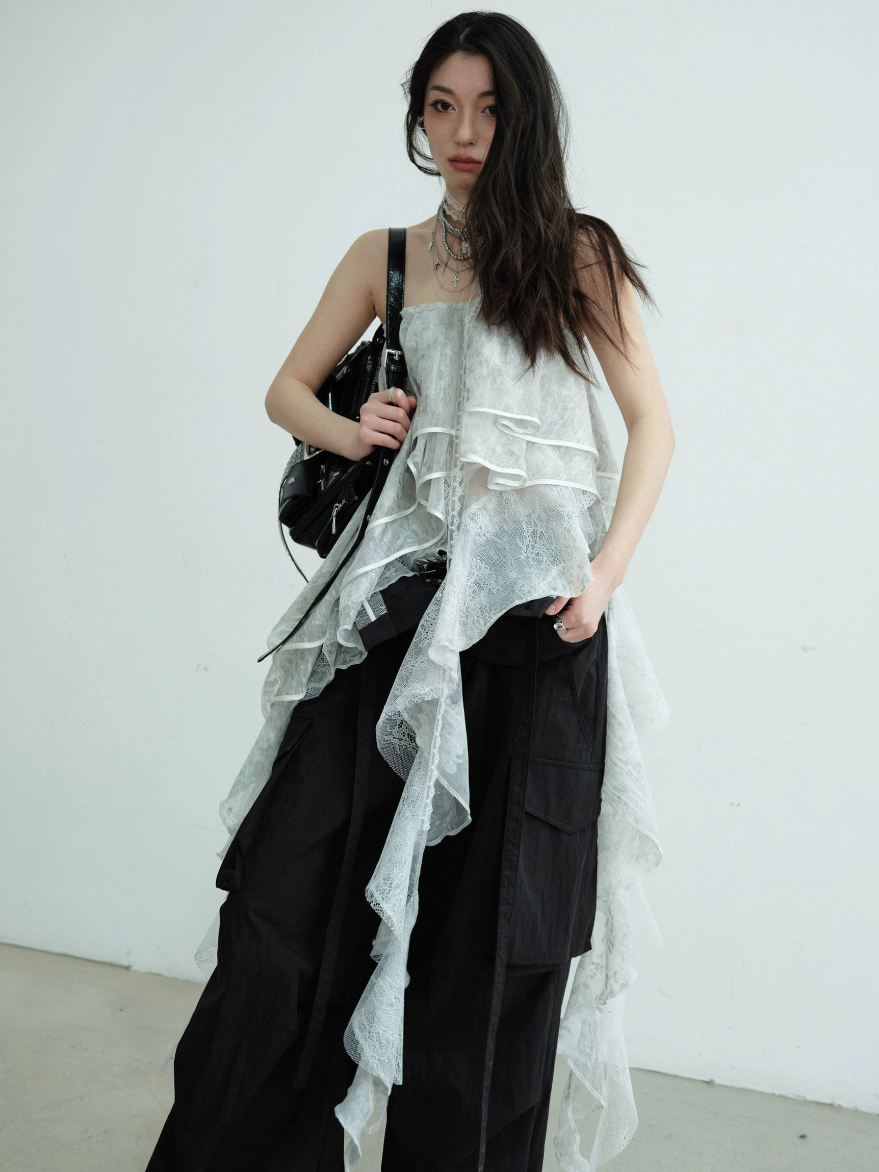 Side view of light gray sheer lace ruffle tube top maxi skirt with an asymmetric cascading draped hem and black crossbody bag