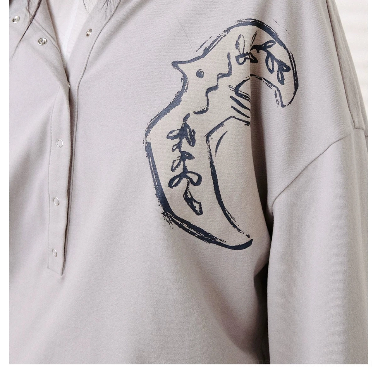 Close-up chest detail of light gray cotton Henley polo shirt with dark blue animal embroidery and half-button neckline
