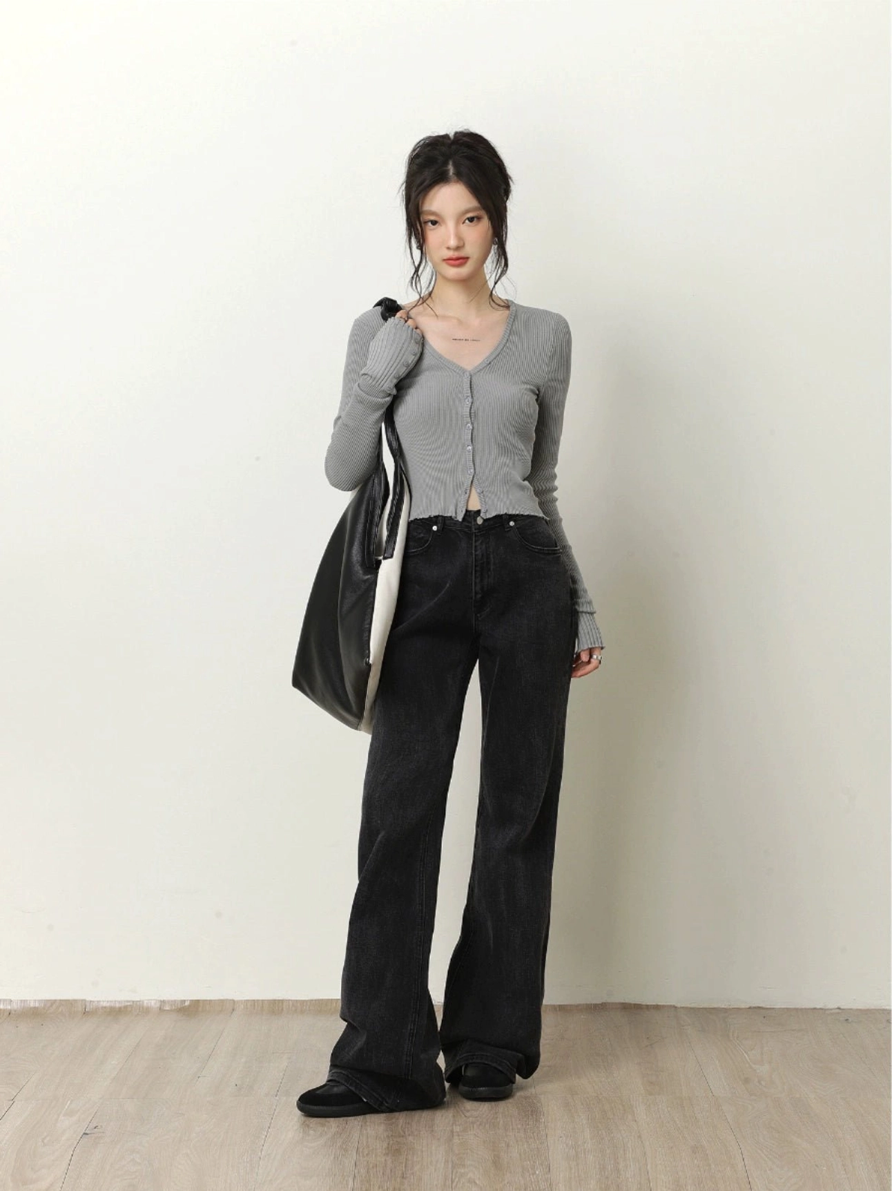 Light gray cropped V-neck ribbed knit cardigan styled with black wide-leg jeans and a tote bag in a minimalist studio