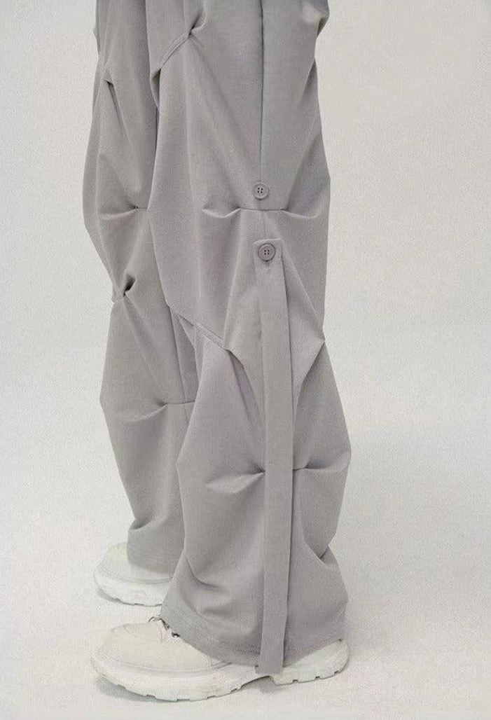 Side view of light gray geo-sculpt wide-leg pants showing gathered pleats decorative side buttons and relaxed streetwear fit