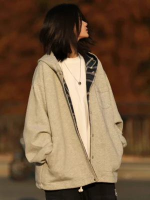 Light gray oversized plaid-lined button-up hoodie jacket shown from a left three-quarter view on a woman in an autumn streetwear setting