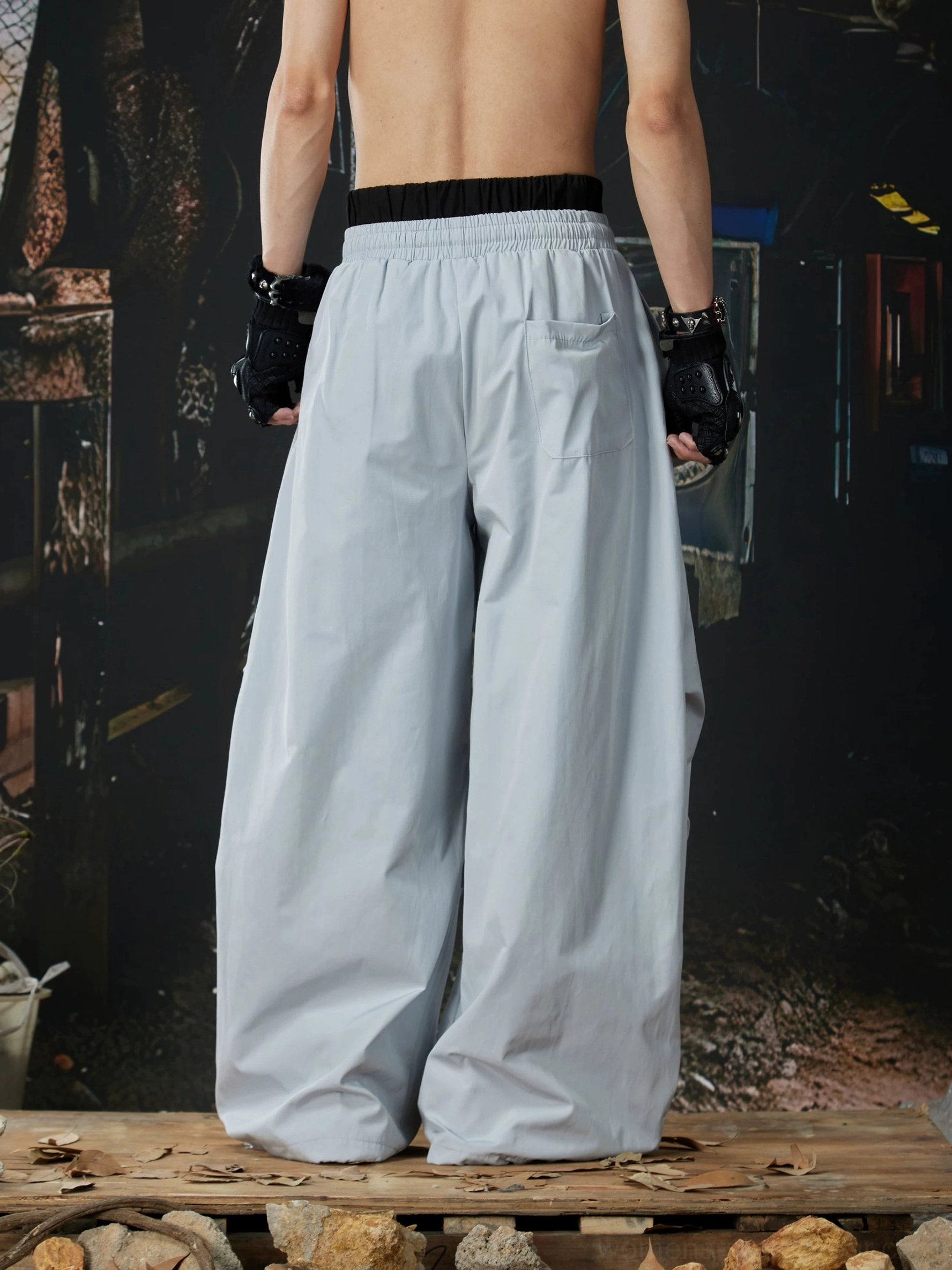 Rear view of light gray oversized track pants with black elastic waistband, smooth fabric, and relaxed wide-leg streetwear silhouette