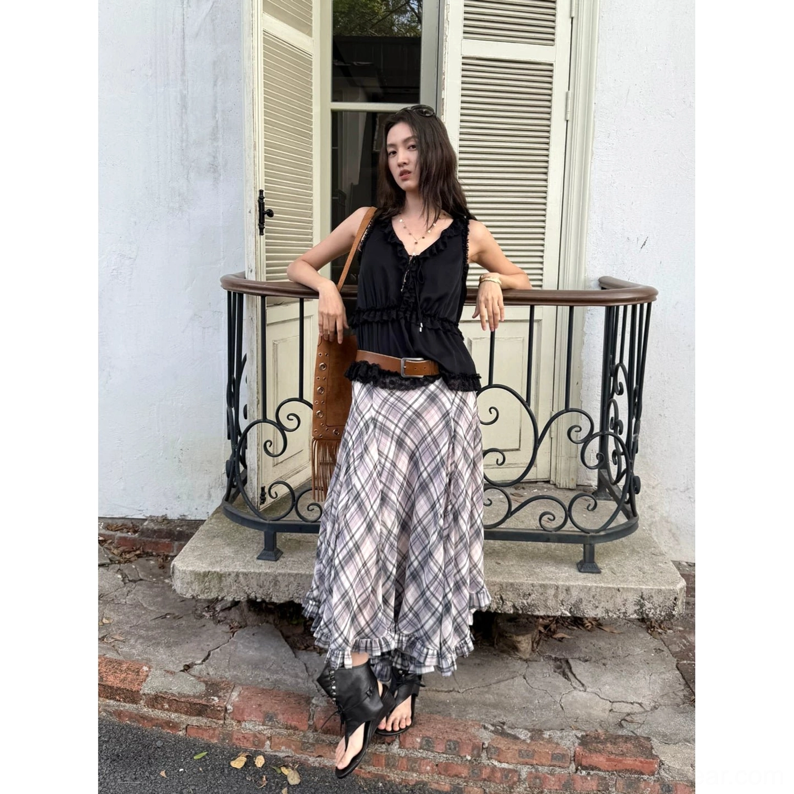 Light gray plaid chiffon asymmetric hem maxi skirt styled with a black camisole and brown shoulder bag on a balcony