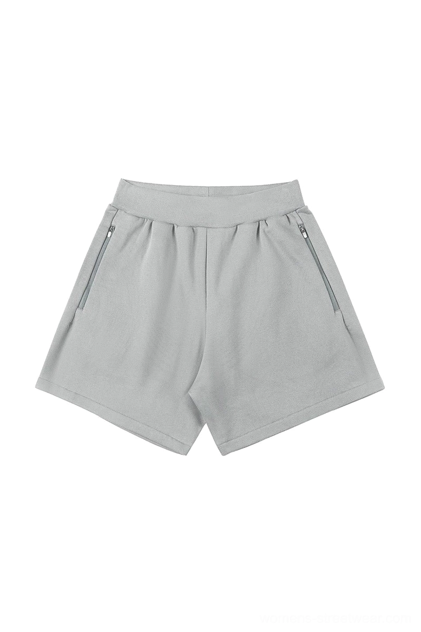 Light gray relaxed unisex streetwear shorts with ribbed elastic waistband and two secure angled zip pockets shown in a flat lay view