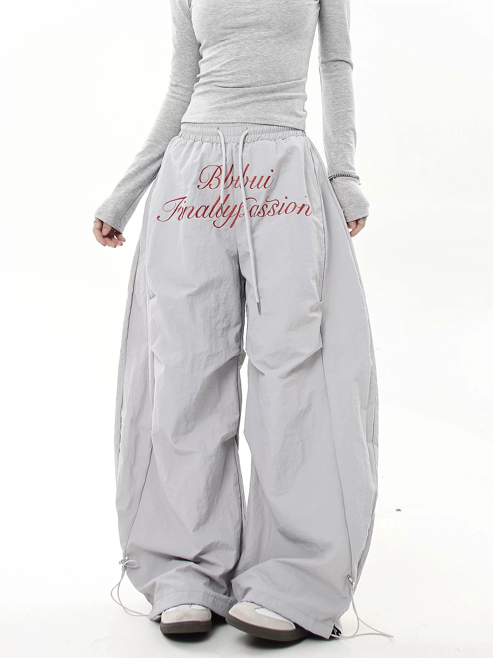 Light gray wide-leg parachute streetwear pants with red cursive embroidery, loose baggy silhouette and adjustable drawcord hems
