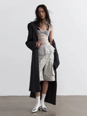 Light gray sheer ruched corset camisole with layered tulle peplum styled under long black trench coat full body view