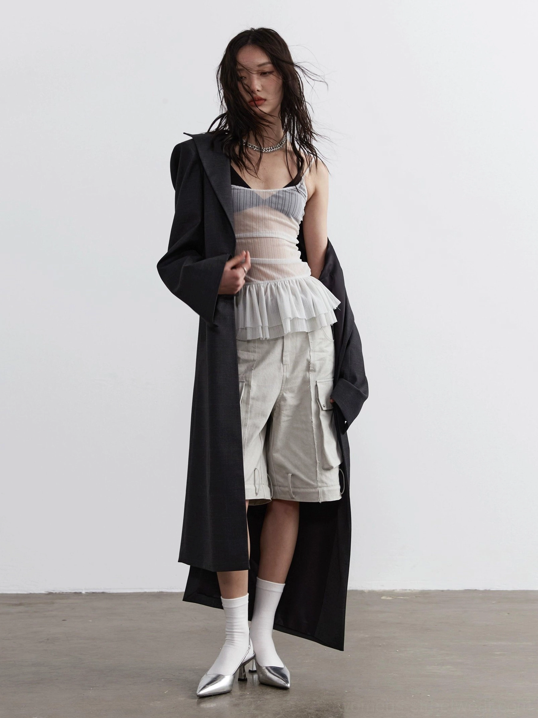 Light gray sheer ruched corset camisole with layered tulle peplum styled under long black trench coat full body view