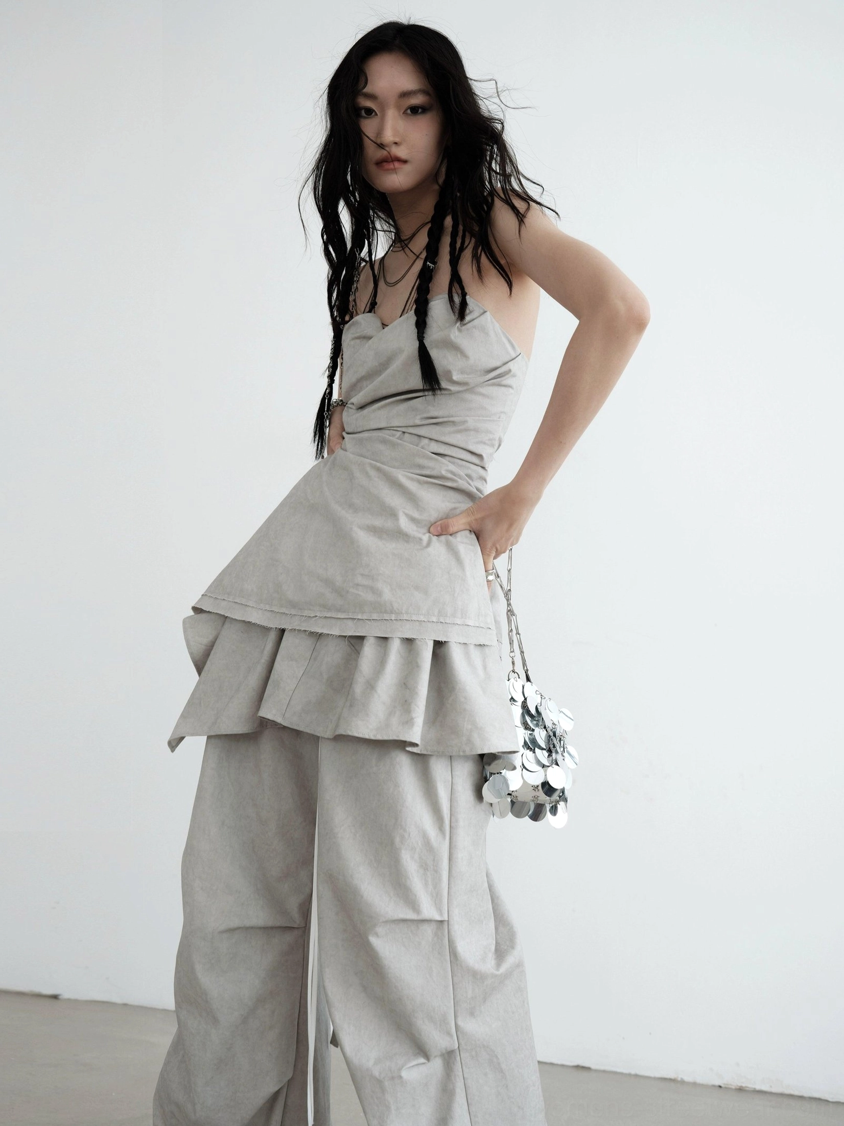 Rear three-quarter view of light gray strapless ruched asymmetric draped top with ruffled layered hem