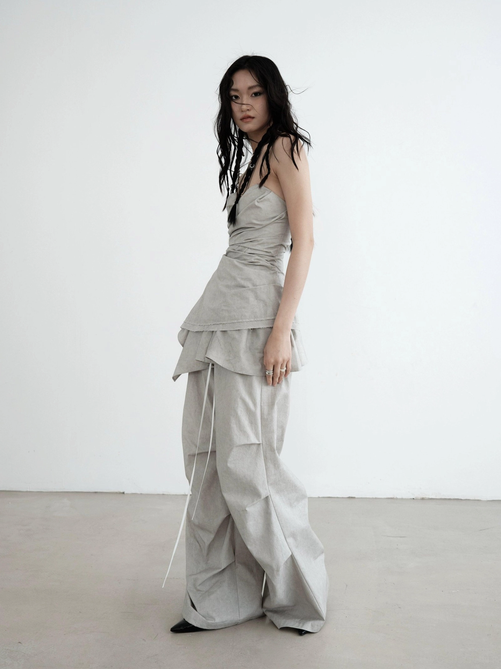 Light gray strapless ruched asymmetric draped top side profile with fitted bodice and sculptural layered waist detail