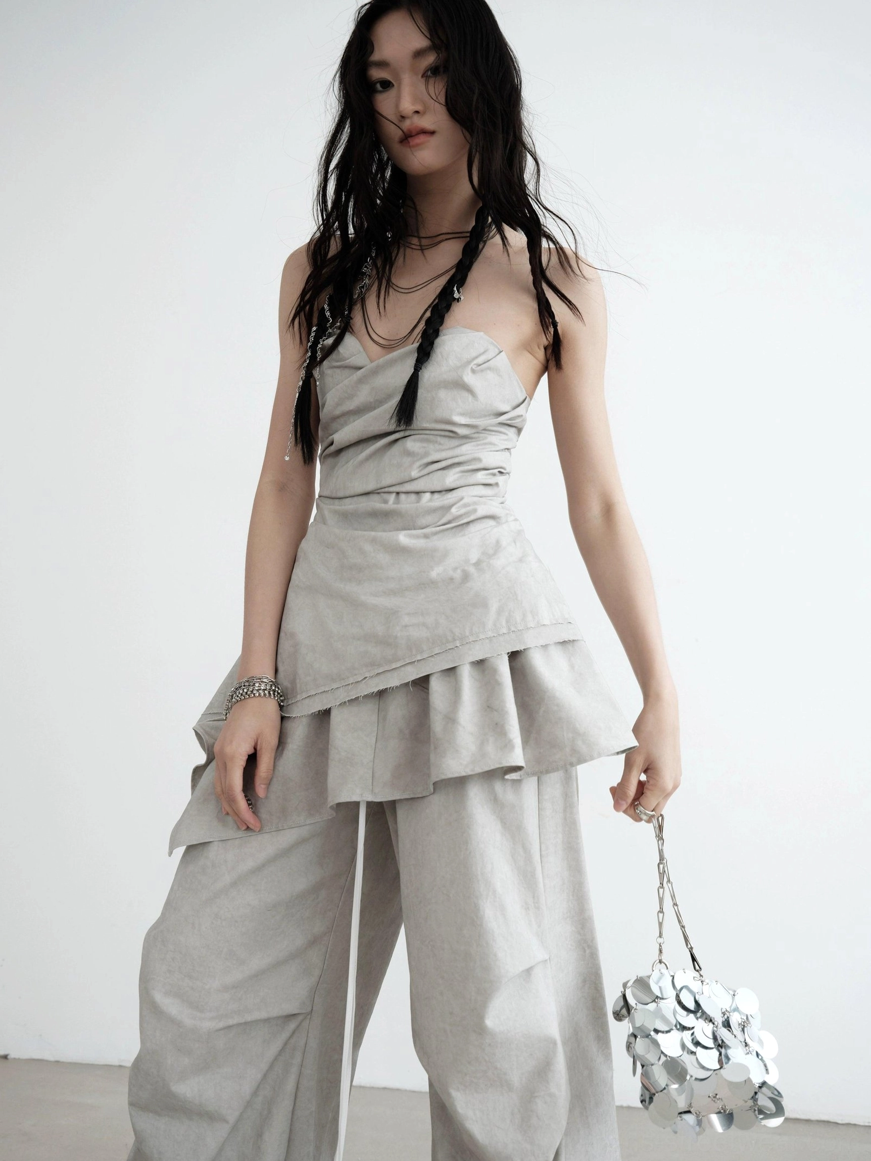 Side view of light gray strapless ruched asymmetric draped top with layered hem styled in a Seoul streetwear look
