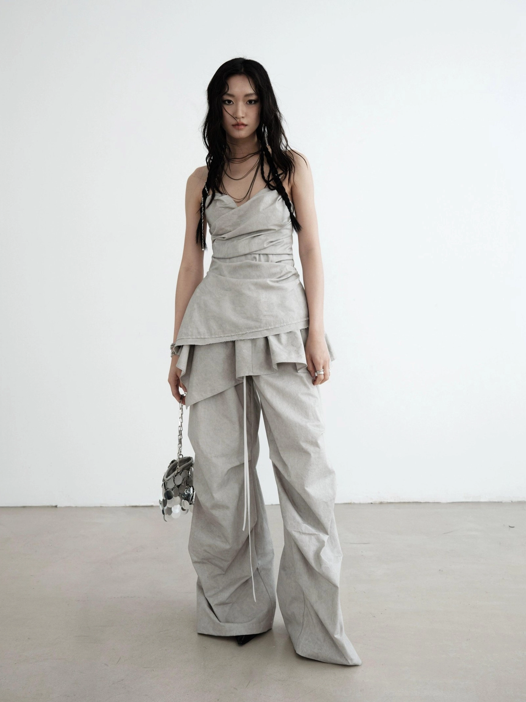 Light gray strapless ruched asymmetric draped top styled with loose cargo pants and silver handbag for Korean streetwear