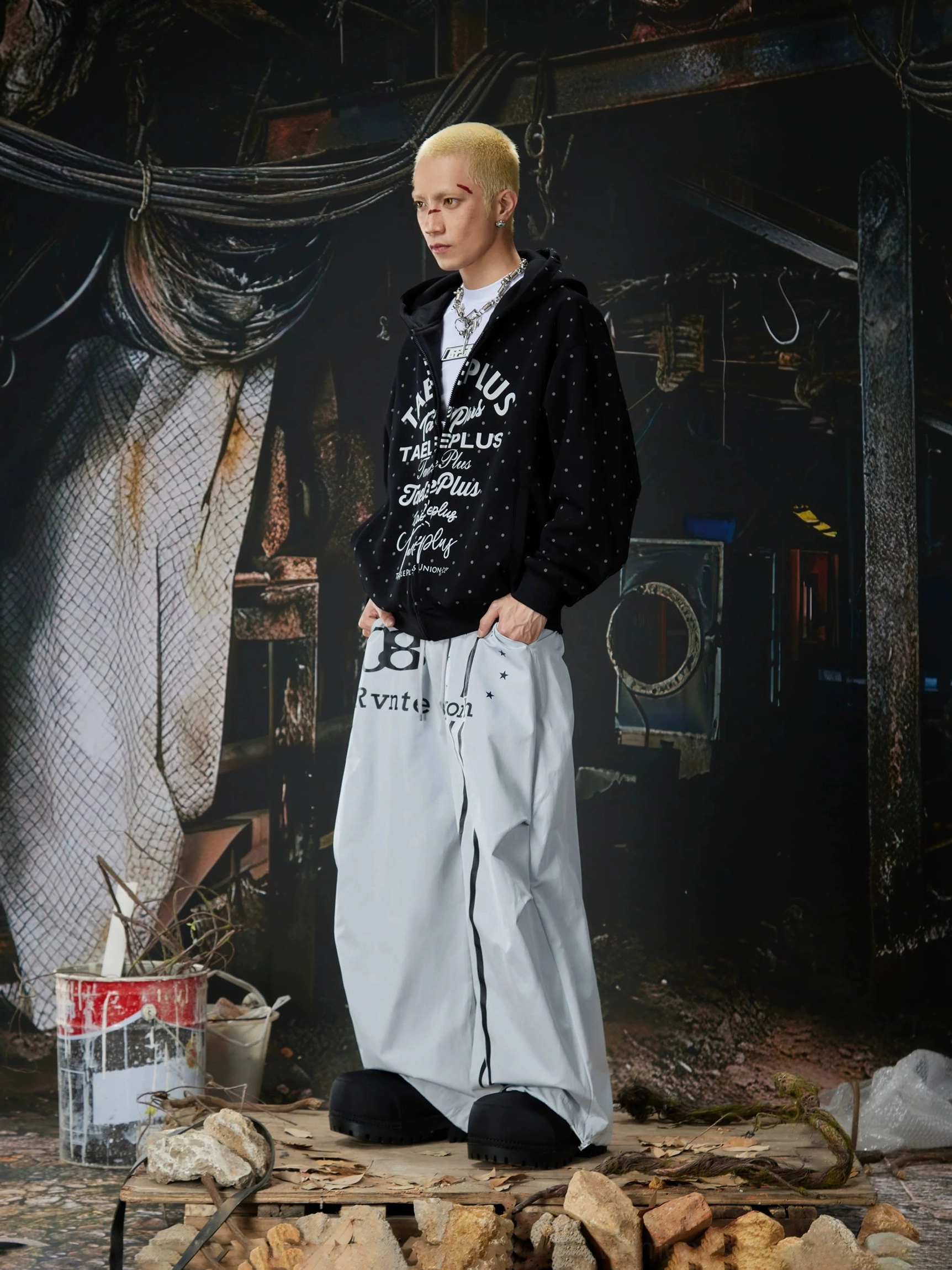 Light gray wide-leg streetwear pants styled with a black graphic hoodie and casual black slippers in a modern urban outfit