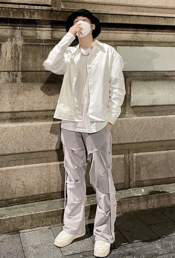 Light gray wide-leg streetwear pants with side drawstrings styled with a white button-up shirt bucket hat and white sneakers