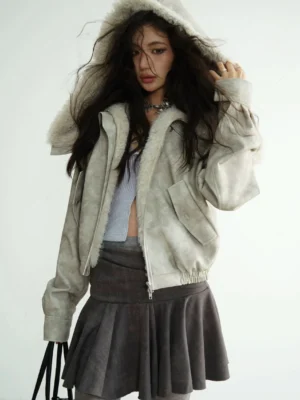 Model wearing a light grey faux shearling hooded cropped jacket with plush fur hood and front zipper in a three-quarter studio view