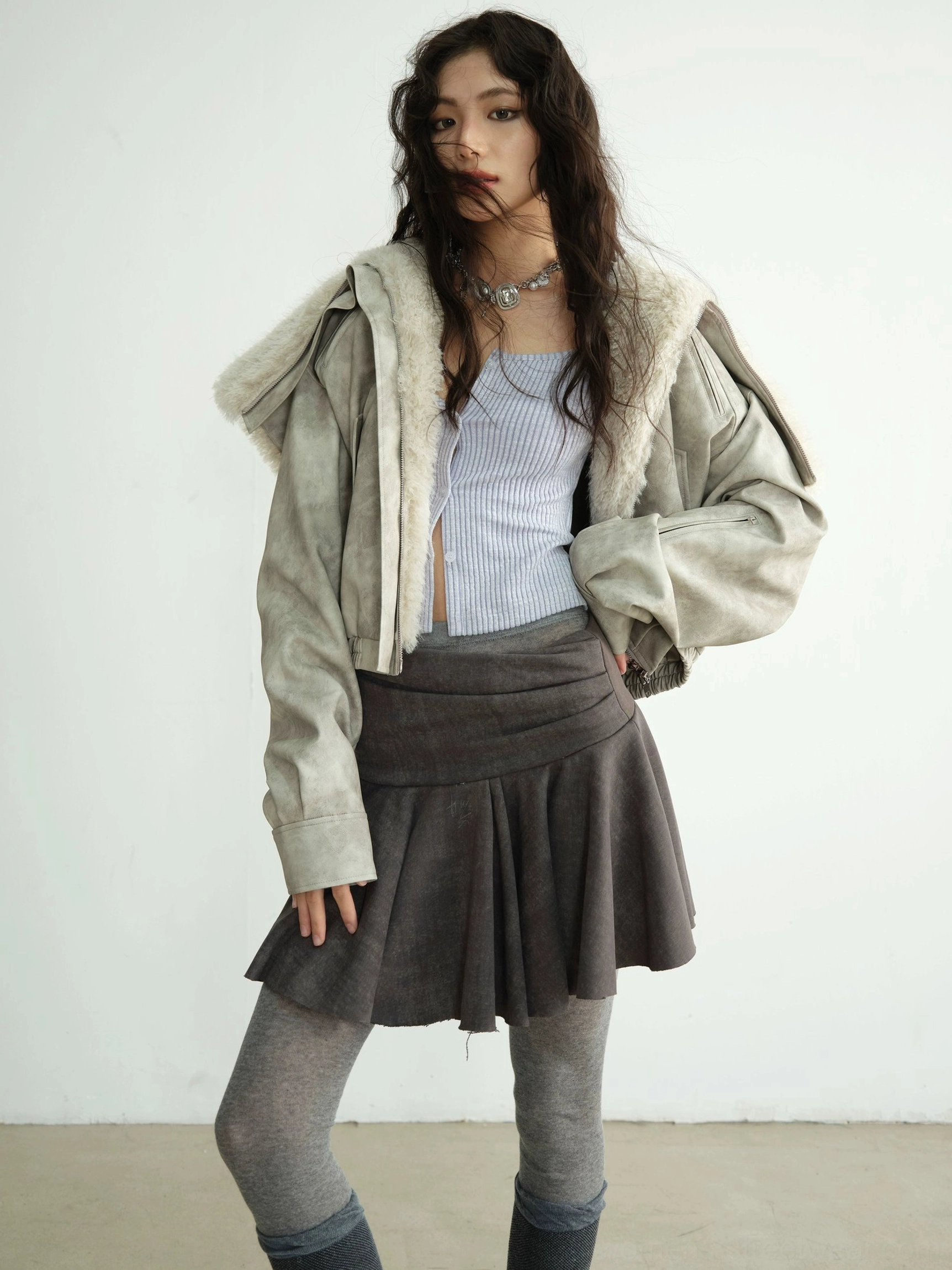 Close-up of a light grey faux shearling jacket with wide fold-over fur collar, hood detail, zipper, and silver necklace styling